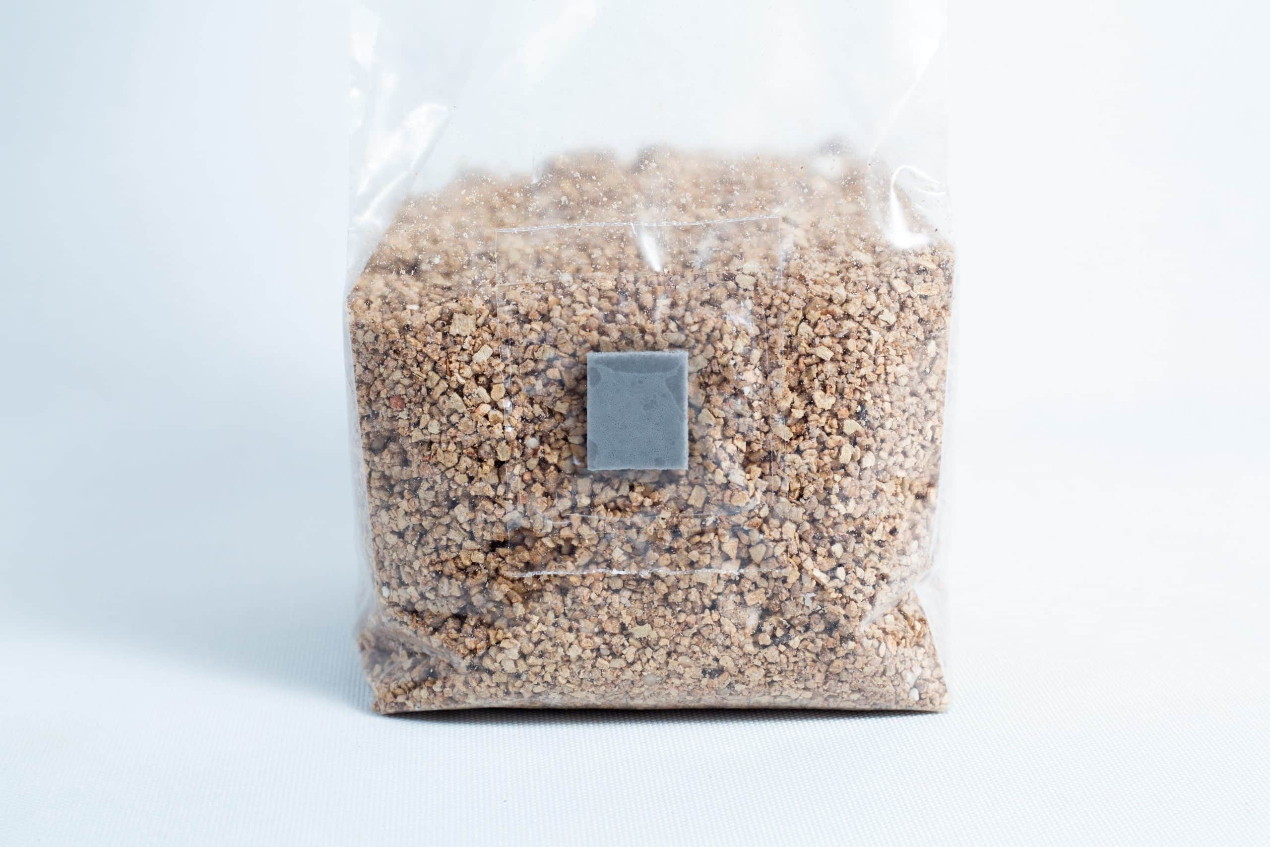 A clear plastic bag of Organic Brown Rice Flour BRF 4X 500g for PF Tek, sealed and upright on a white surface, filled with small brown granules.