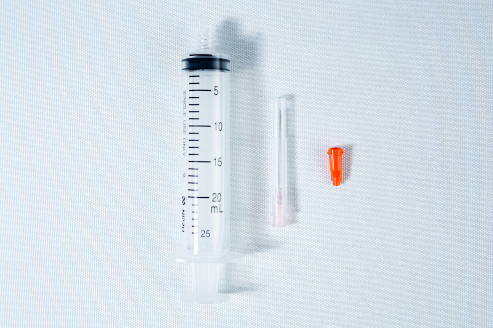 A 25 mL syringe, a needle, and an orange cap on a white background.