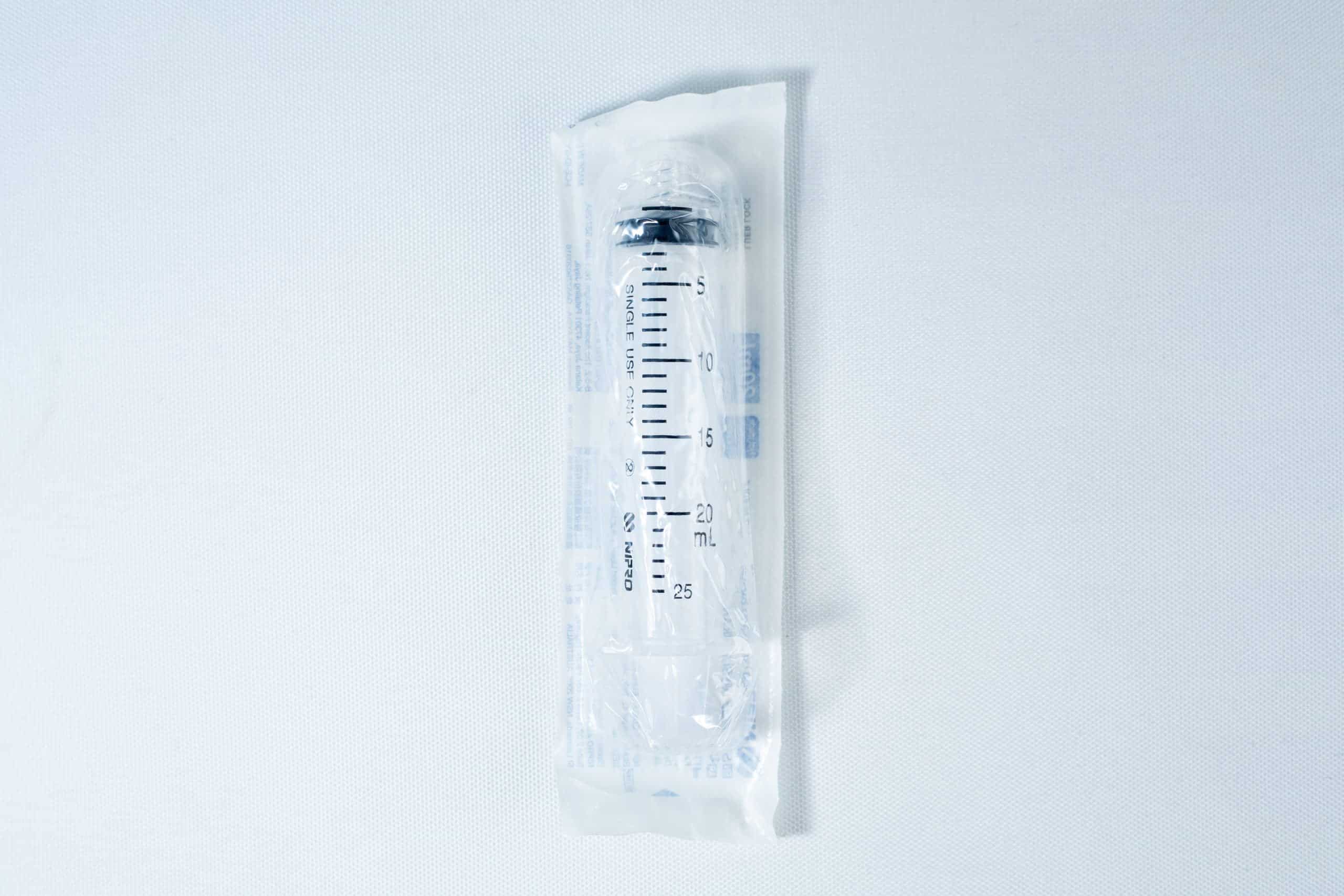 A packaged disposable syringe lies on a white surface, sealed in transparent plastic wrapping.