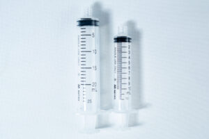 Two clear plastic syringes, one large and one small, placed side by side on a white background.