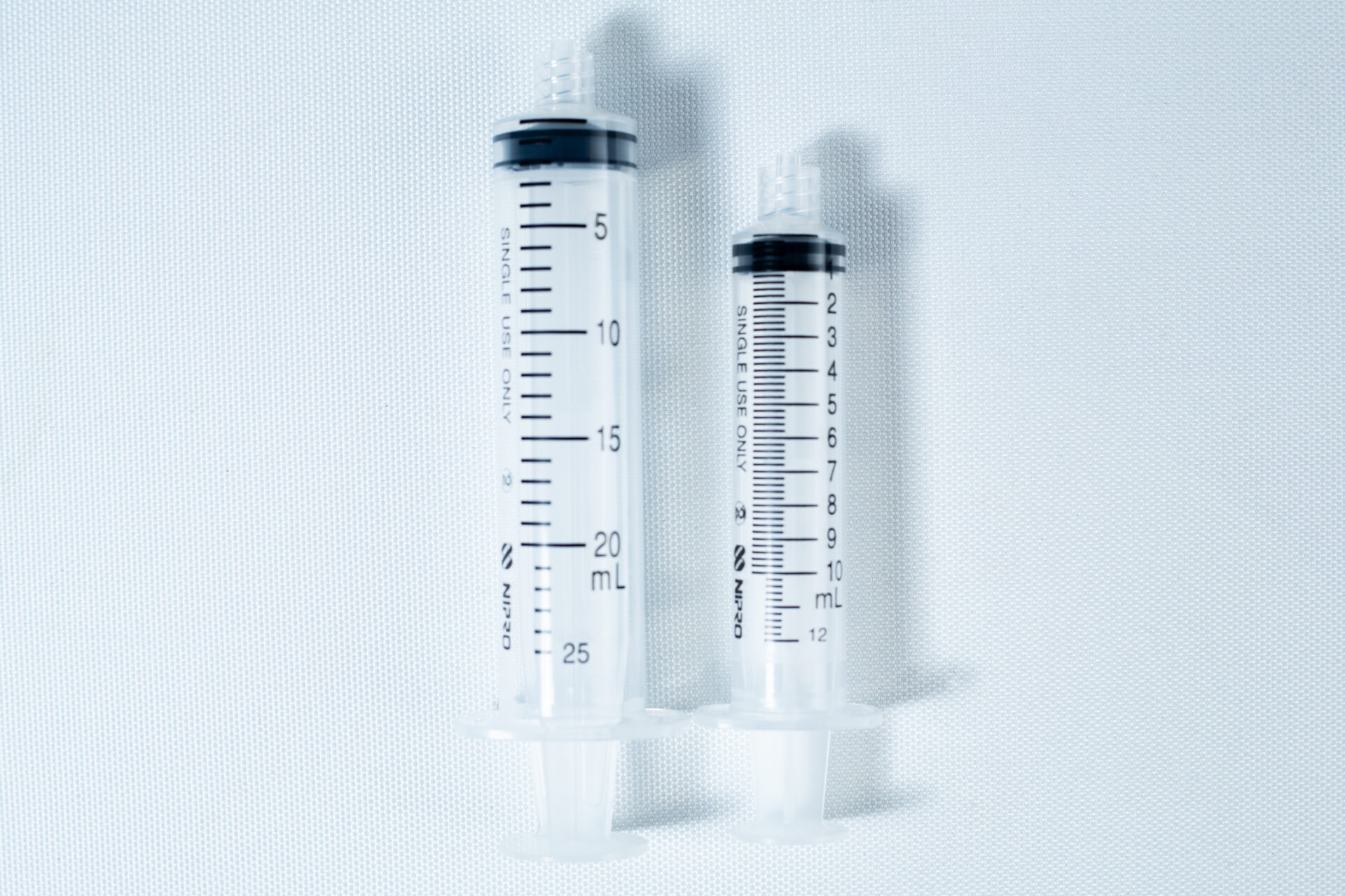 Two clear plastic syringes, one large and one small, placed side by side on a white background.