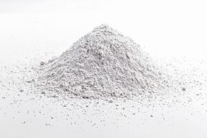 A small mound of Calcium Carbonate for Mycology, a fine white powder, is scattered on a white surface with a plain background.