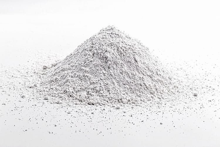 A small mound of Calcium Carbonate for Mycology, a fine white powder, is scattered on a white surface with a plain background.