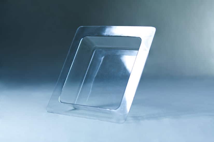 A square, transparent plastic tray with a raised rim, inspired by the Mycelium Mould Growth form - Paver (Reusable), sits elegantly on a light blue surface and background.