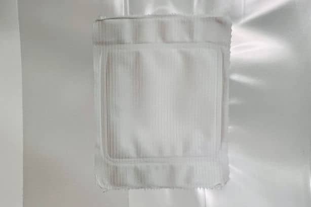 A white, square gauze pad is attached to a white, shiny surface.