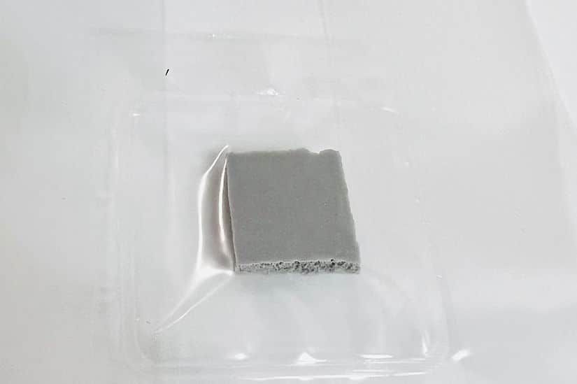 A small, square piece of grey material on a clear plastic tray against a white background.