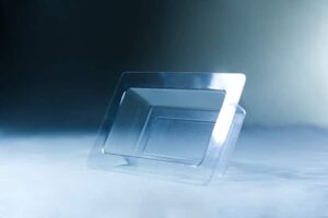 A Mycelium Mould Growth form -Brick (Reusable) stands upright on a smooth, misty surface, its organic curves reflected in the transparent plastic food container lid beside it.