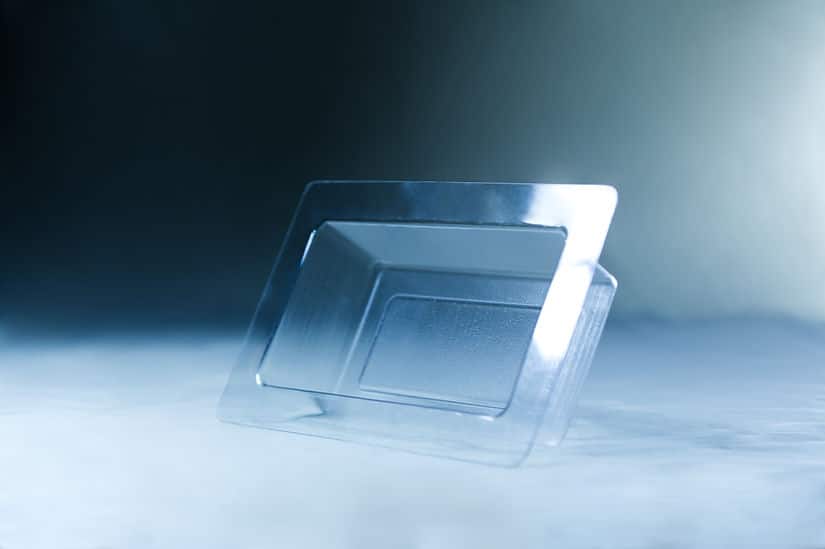 A Mycelium Mould Growth form -Brick (Reusable) stands upright on a smooth, misty surface, its organic curves reflected in the transparent plastic food container lid beside it.