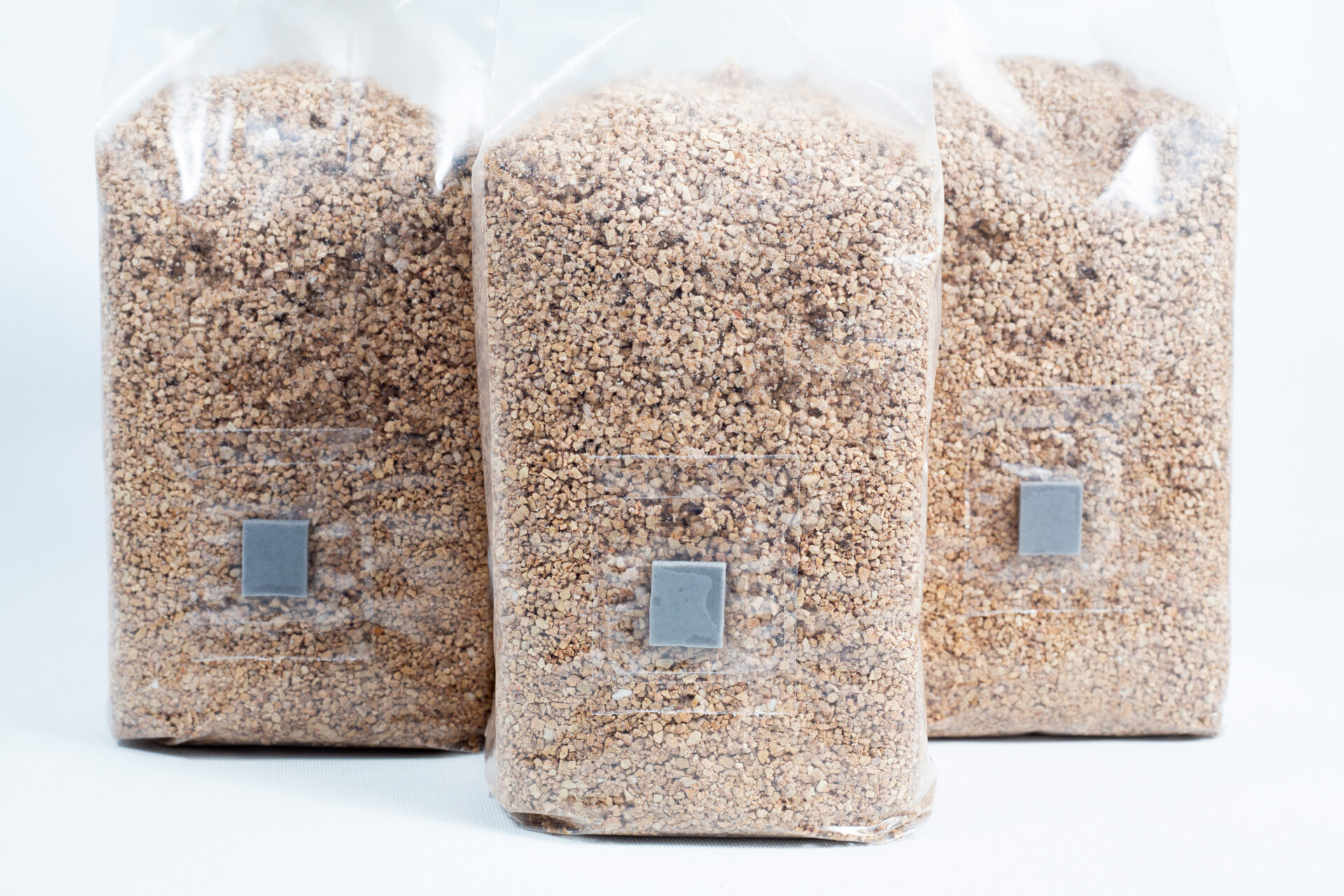 Three 1kg bags of organic brown rice flour (BRF) and vermiculite for PF Tek mushroom cultivation stand upright on a white background.