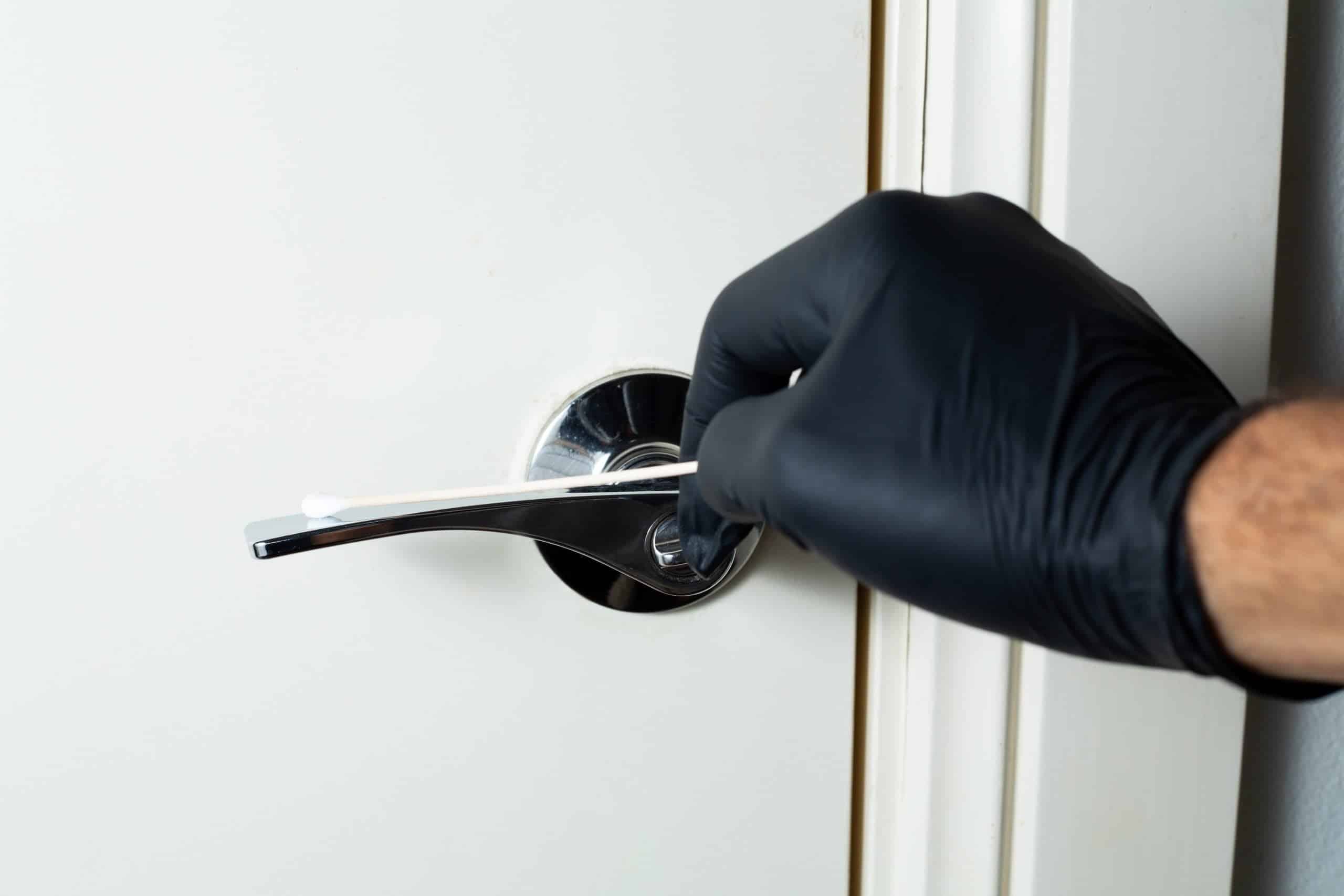 A gloved hand holds a cotton bud near a door handle, likely collecting evidence for a school experiment using the Agar Petri dish MEA School Science Fun Project Kit.