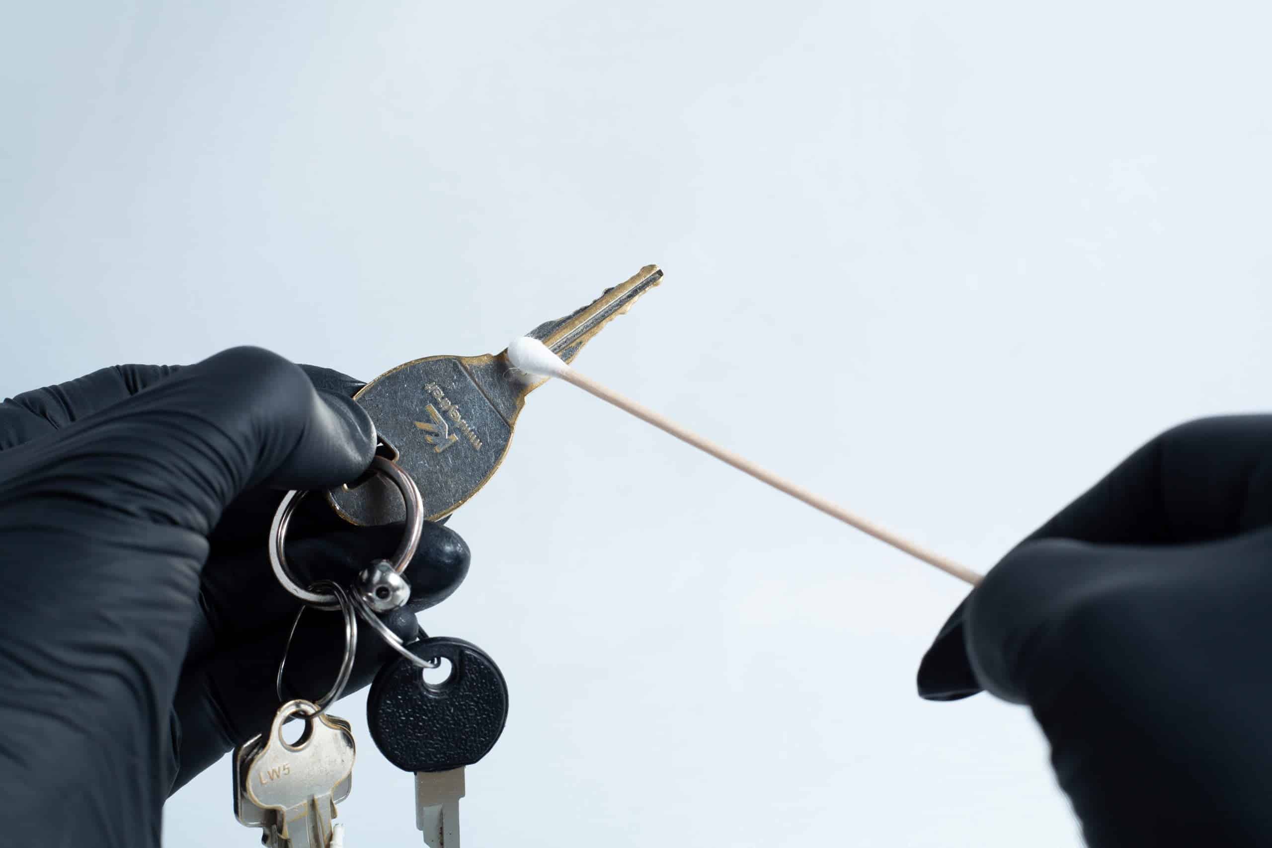 Gloved hands clean a house key with a cotton bud against a plain light background, just like using the Agar petri dish MEA School Science Fun Project Kit for school experiments or science fun activities.