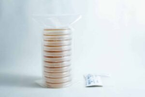 A stack of pre-poured MEAG agar plates (antibacterial) 90mm, sealed in plastic, sits next to a small packet on a white surface.