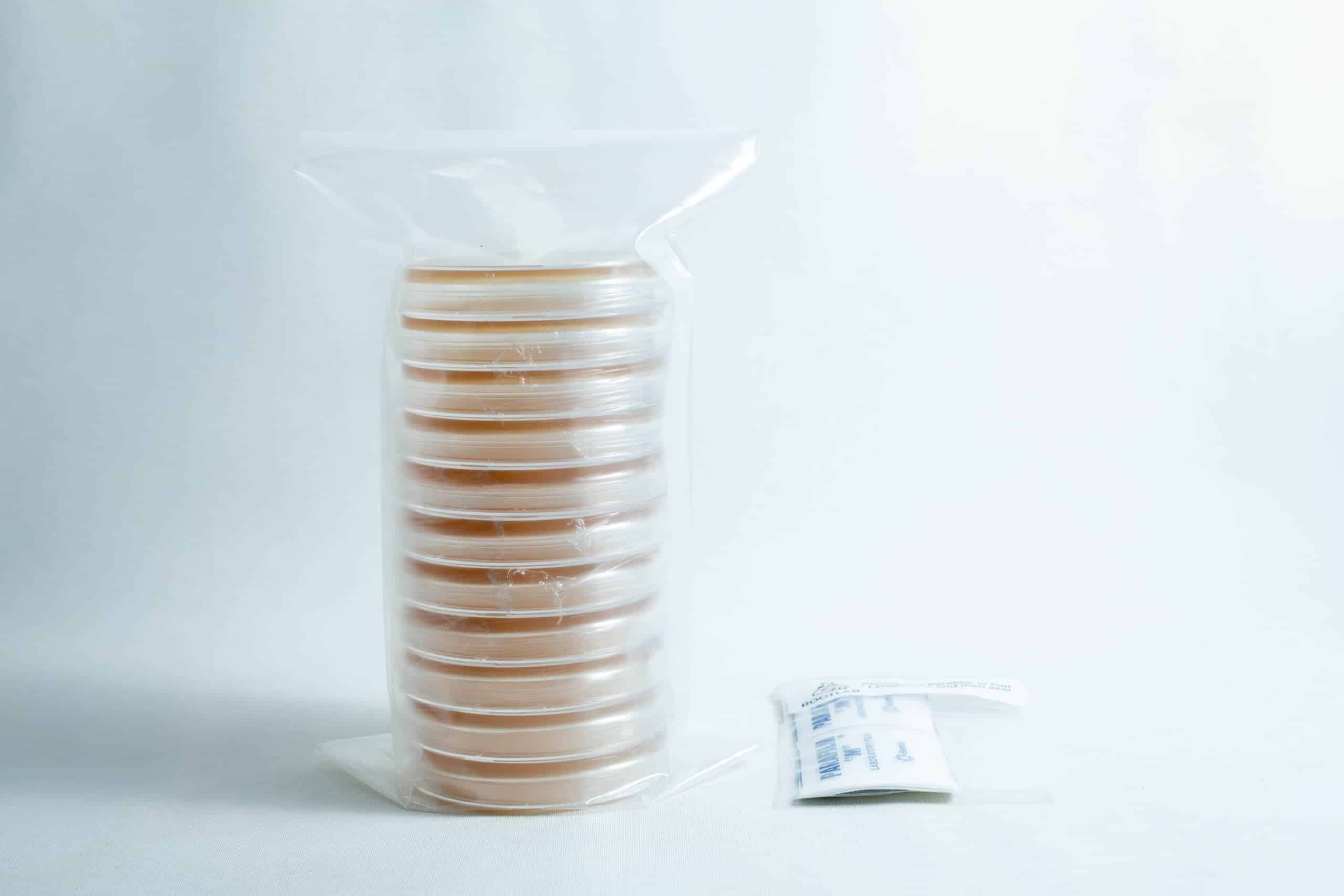 A stack of pre-poured MEAG agar plates (antibacterial) 90mm, sealed in plastic, sits next to a small packet on a white surface.