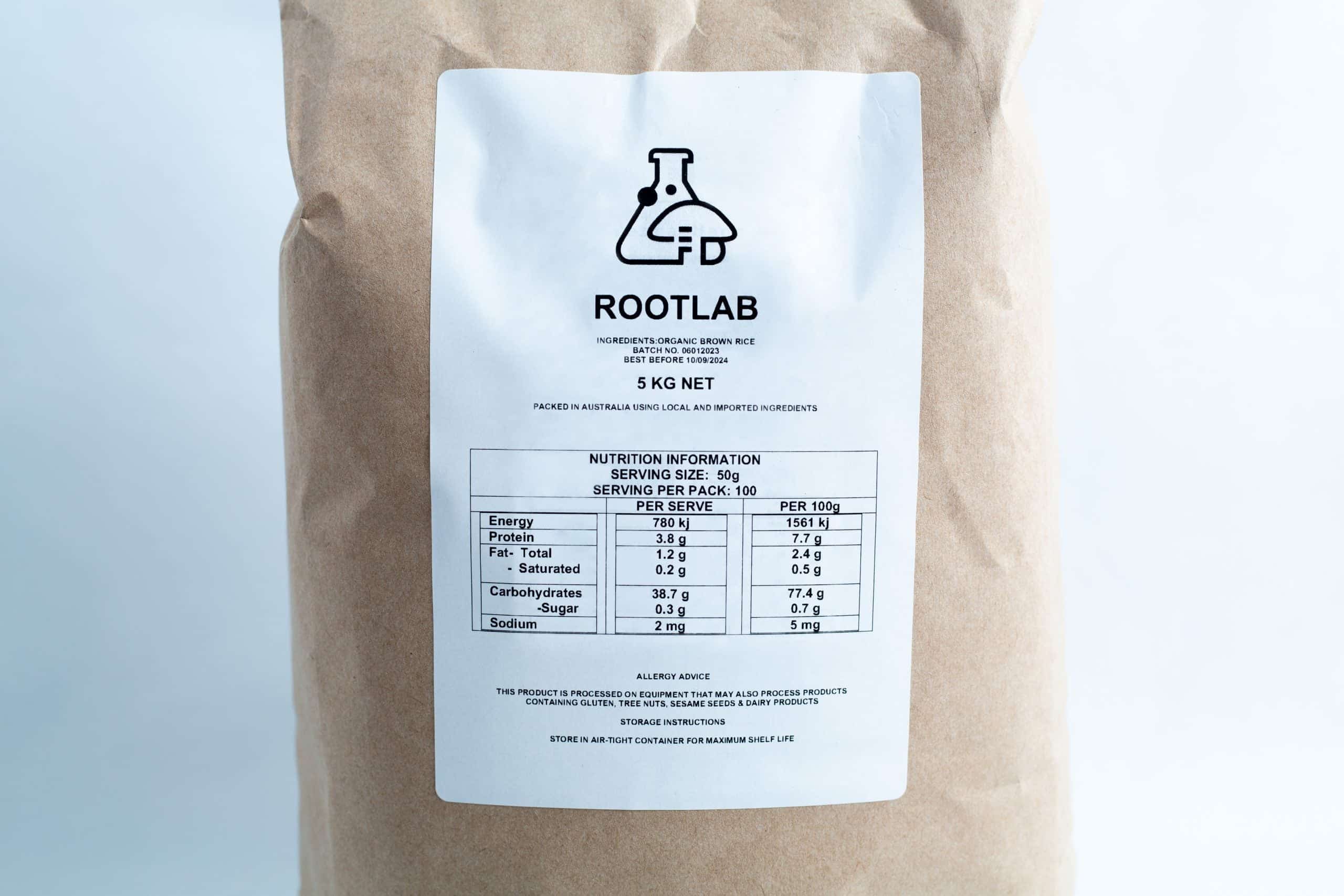 A brown paper bag labelled ROOTLAB with a nutrition information table, science beaker logo, and "Brown Rice Flour 5kg Organic Food Grade" printed on the front.