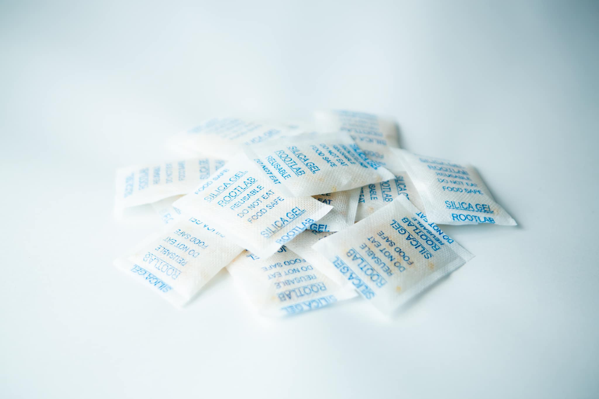 Desiccant Silica Gel 5g | Reusable sachets with blue writing are arranged on a white surface.