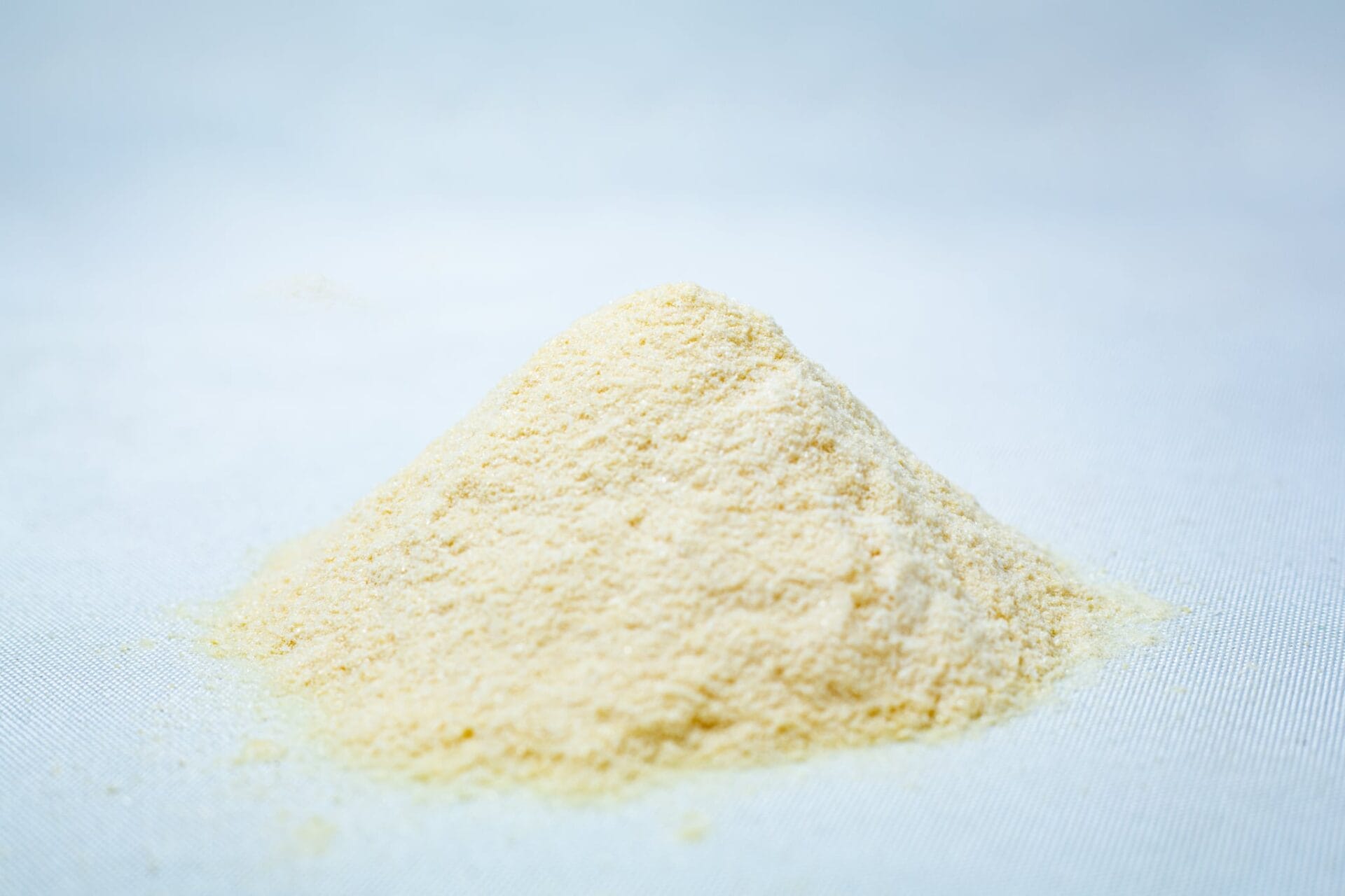 A small mound of pale yellow Liquid Culture Pre-mix | DLME | Now Extra Clear powder rests on a white surface, set against a light blue background.