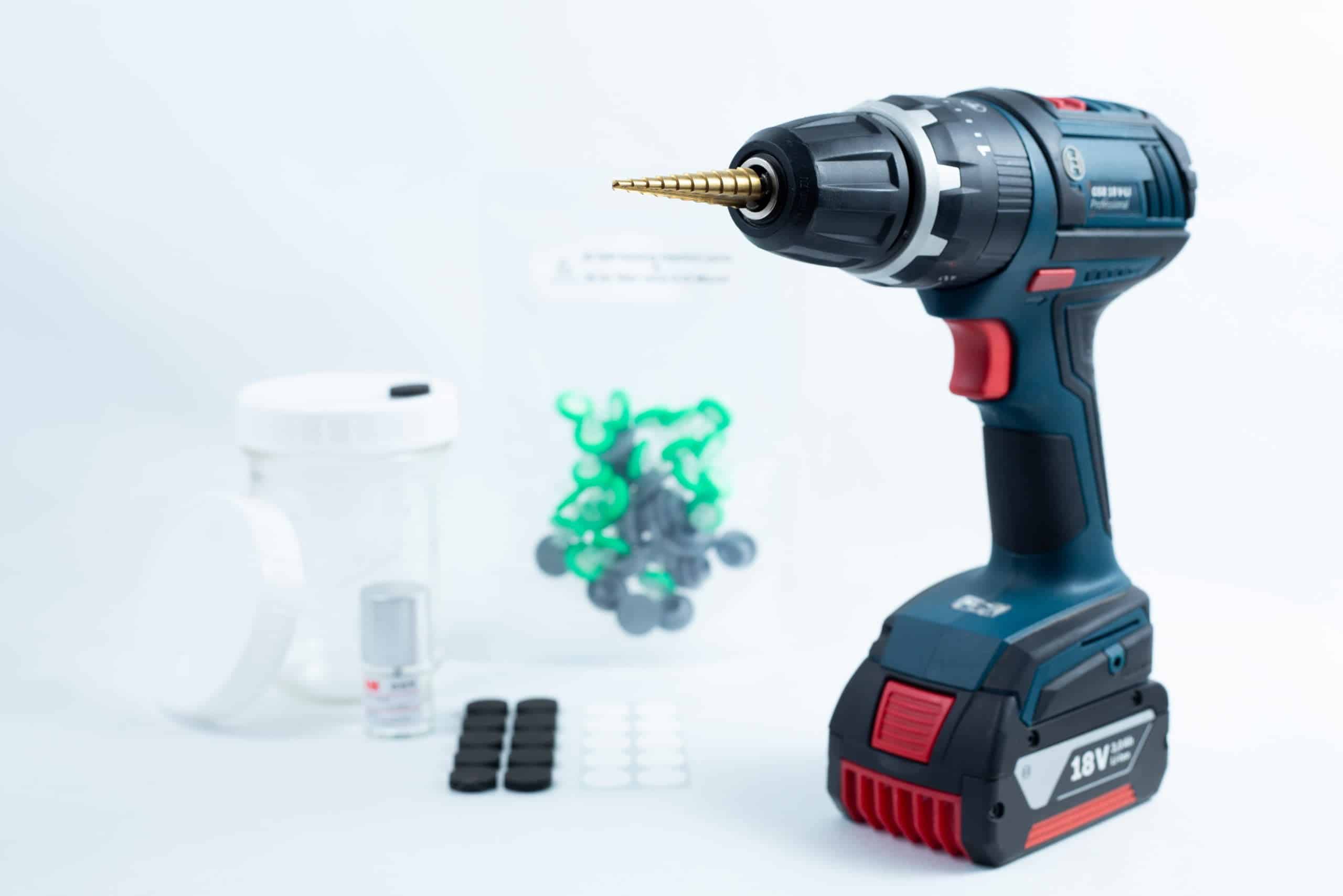 A Drill Bit for holes size 3mm–12mm Titanium Coated rests beside small containers and plastic pieces on a white surface.
