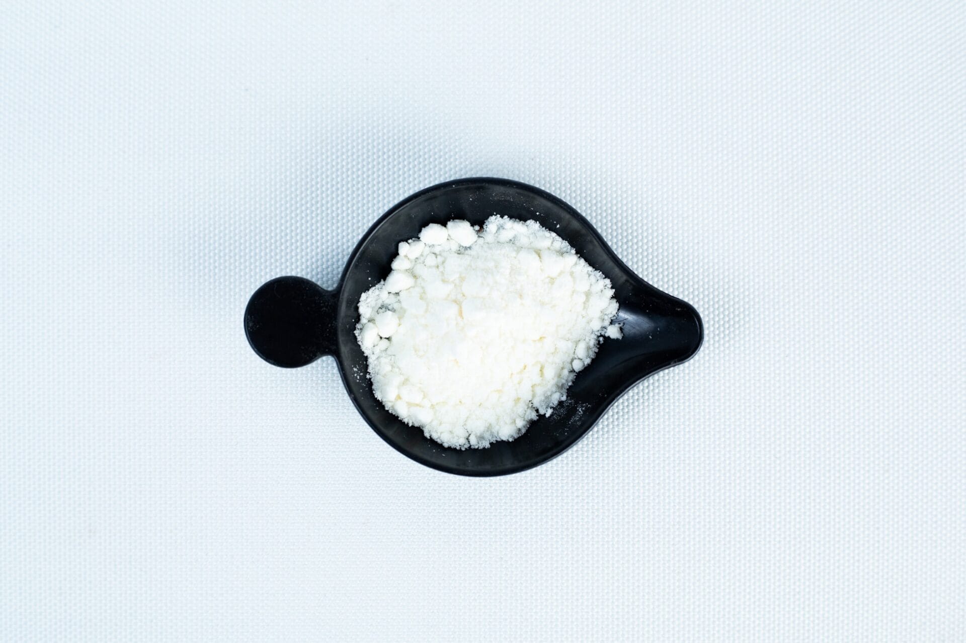 A black bowl containing Antibacterial Powder for mushroom cultivation sits on a white textured surface.