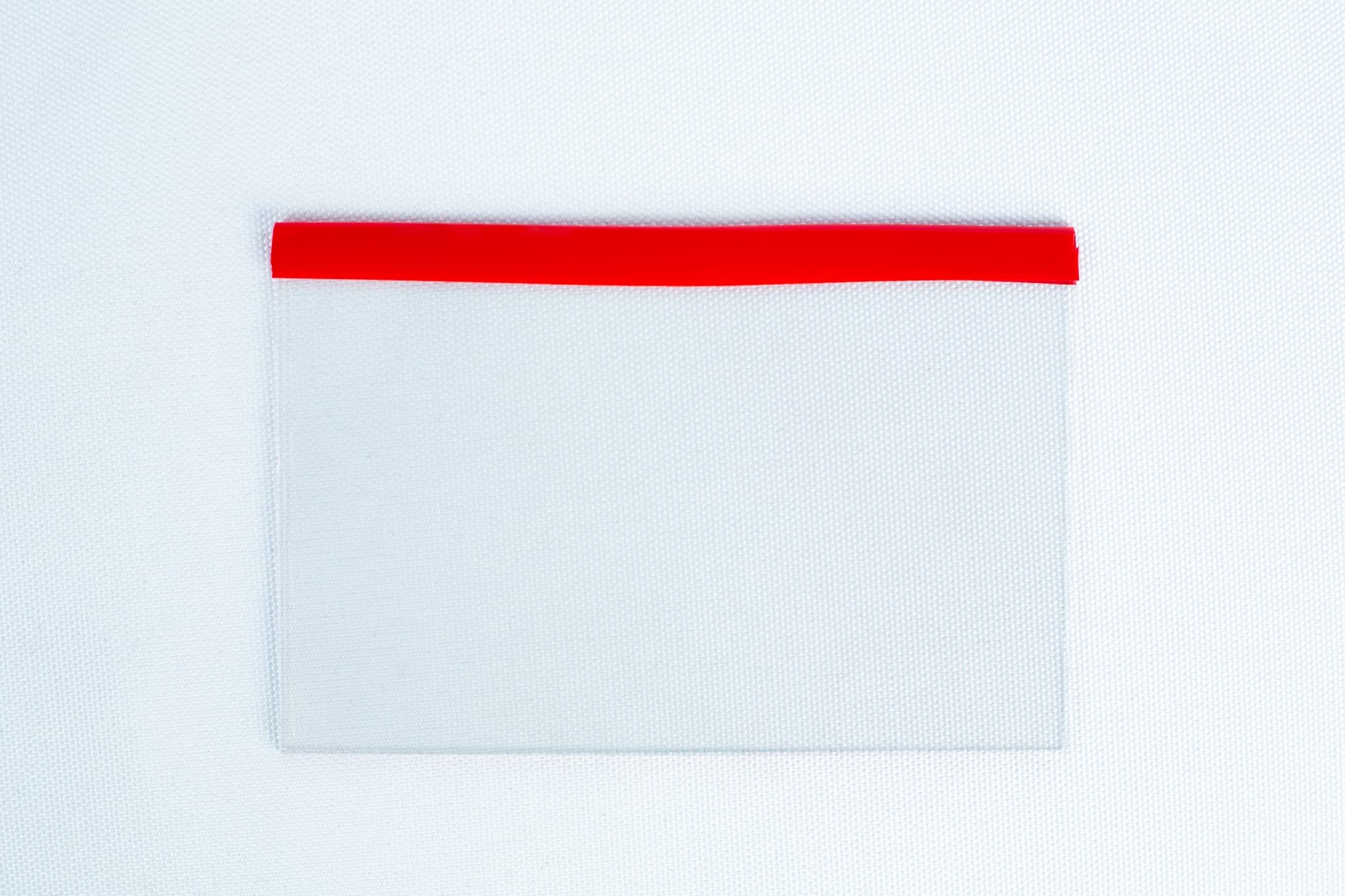 A transparent pocket with a red top edge on a white textured background is perfect for storing the Glass Spore Print Slides booklet (12.8cm x 8.5cm x 1mm) to safely preserve spore prints.