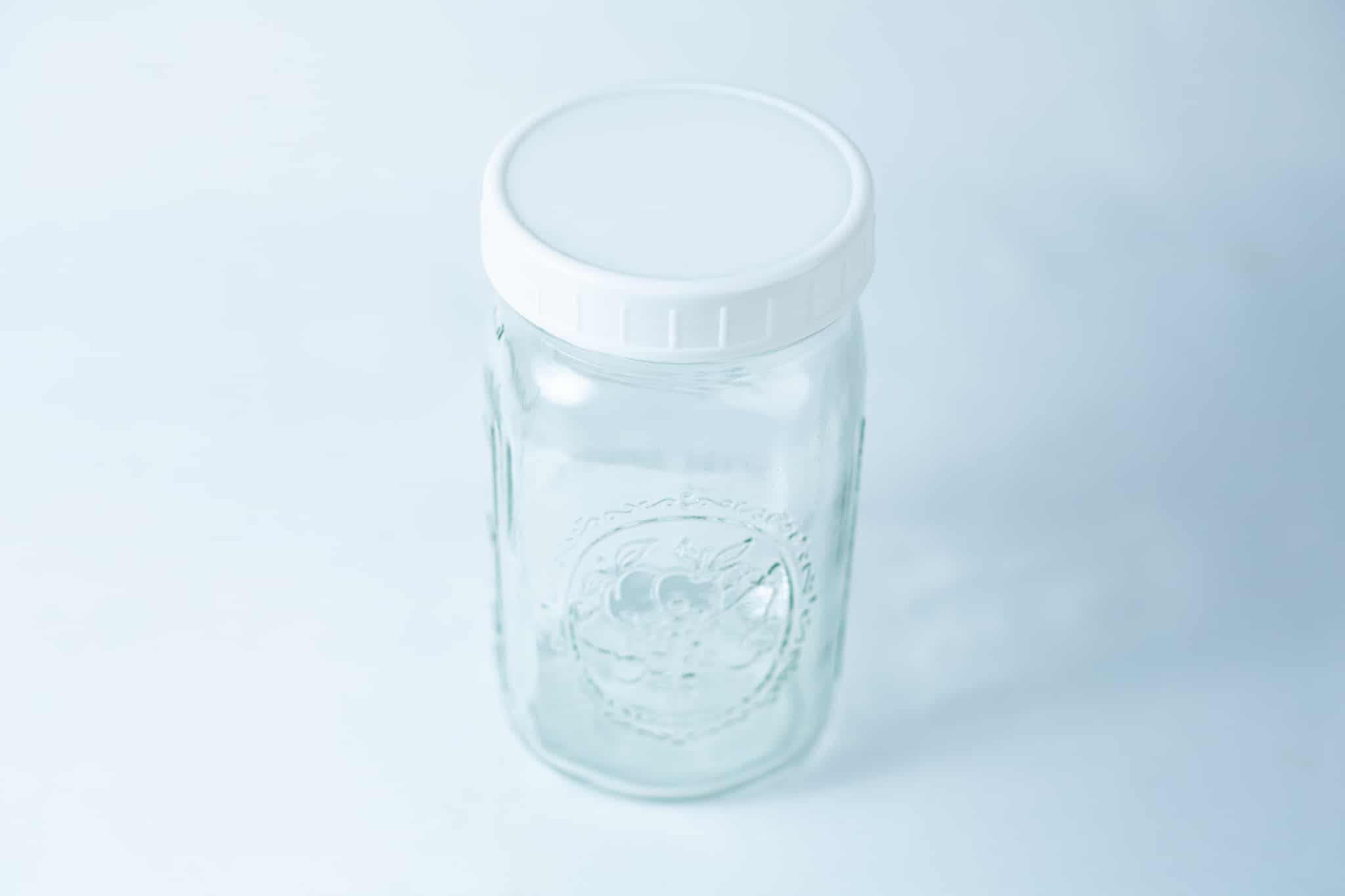 Photographed on a light blue background, this clear glass jar features a plain white plastic lid, designed to fit wide mouth mason jars with 86mm Mason Jar Lids | Wide Mouth | Plain White Plastic Lids.