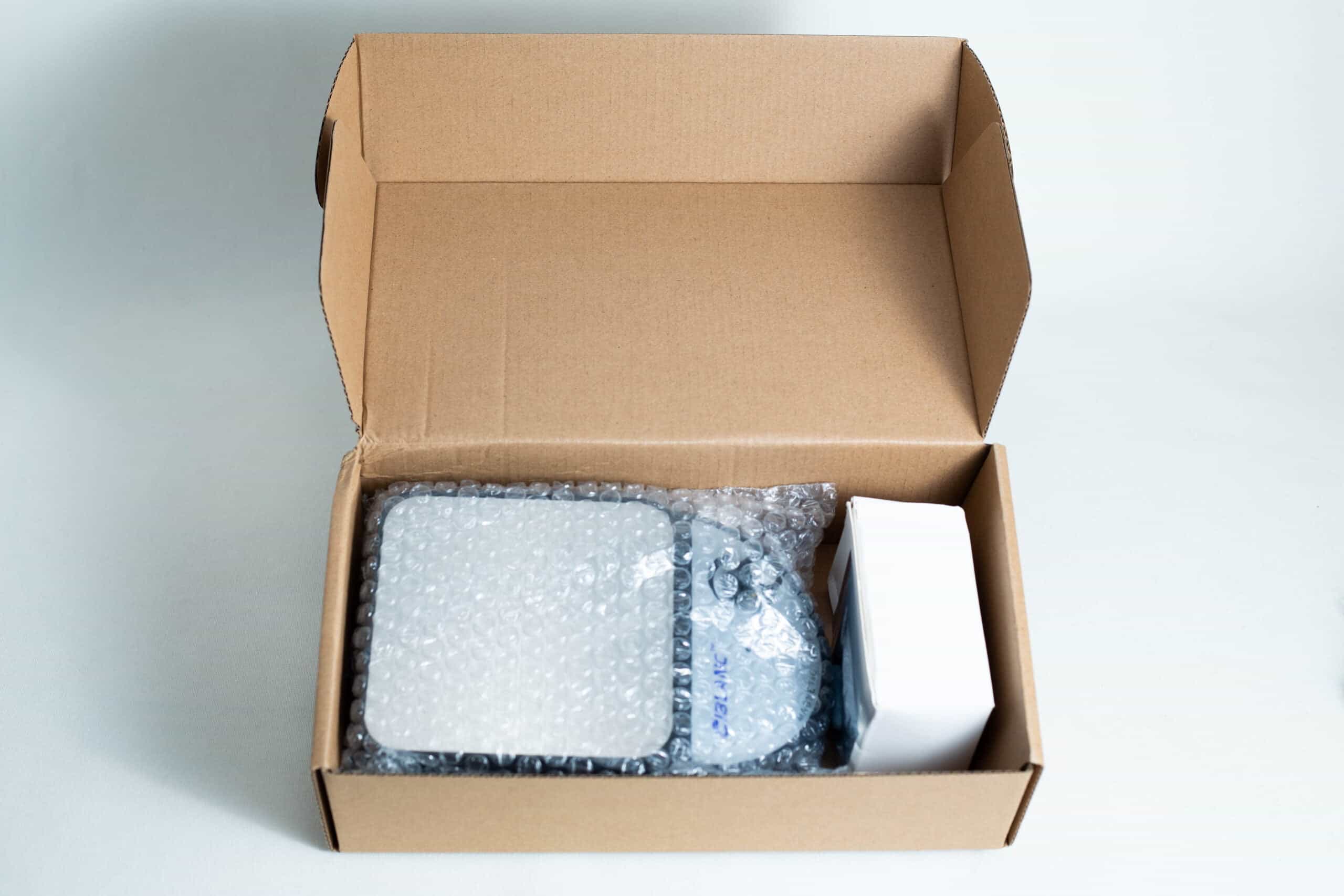 Open cardboard box with bubble-wrapped items and a white rectangular box inside, possibly containing the Magnetic Stirrer Ciblanc 3500rpm—ideal for anyone seeking magnetic stirrer equipment. All items are neatly arranged on a white surface.