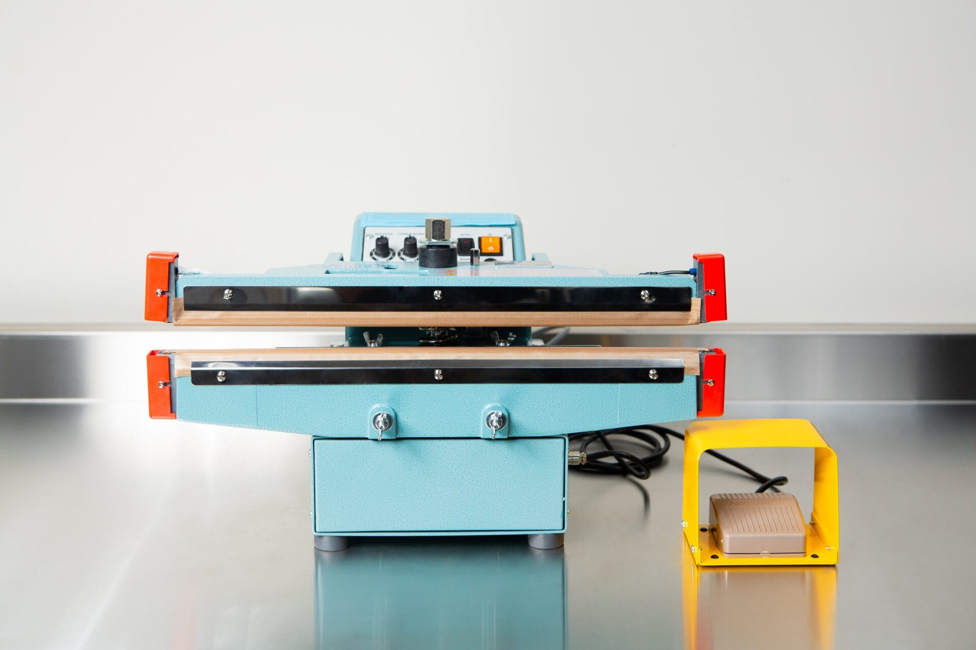 A Heat Sealer 450mm with 10mm Seal | Benchtop Model, featuring control knobs and a yellow foot pedal, sits on a metal counter, designed for reliable industrial sealing.