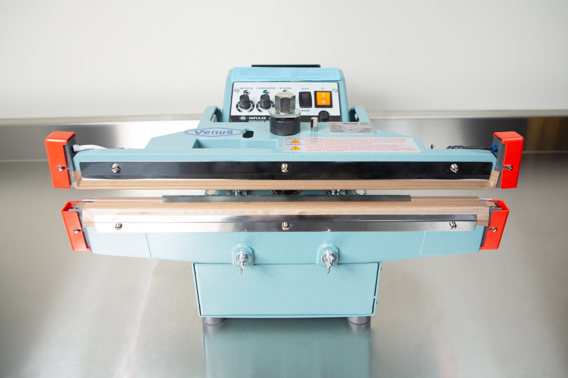 The Heat Sealer 450mm with 10mm Seal | Benchtop Model features a blue body, control panel, and orange clamps on a metal surface, offering efficient industrial sealing with its 450mm heat sealer.