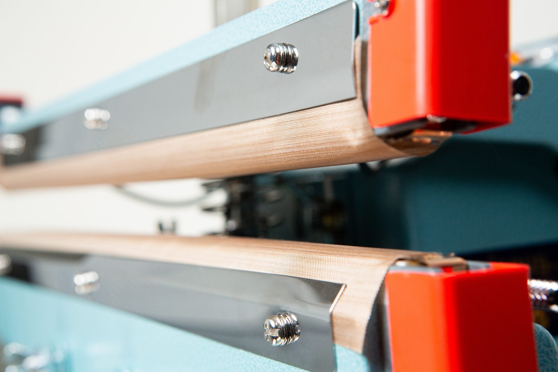 Close-up view of industrial machine parts with metal bars and red components, featuring the Heat Sealer 450mm with 10mm Seal | Benchtop Model for efficient sealing operations.