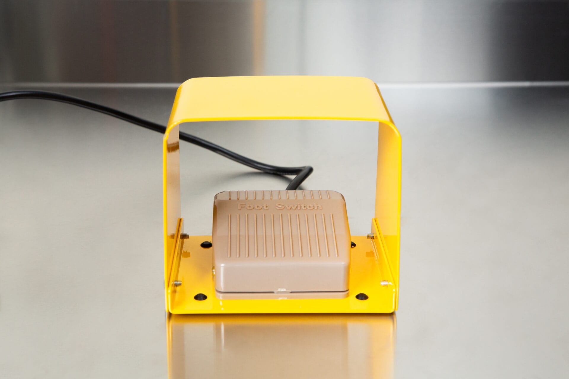 A beige footswitch under a yellow cover rests on a stainless steel surface, ready to operate the Heat Sealer 450mm with 10mm Seal | Benchtop Model.