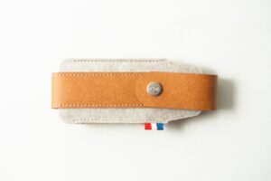 The Opinel Sheath - Brown, made from tan leather and grey felt with a button fastening, rests on a white surface.