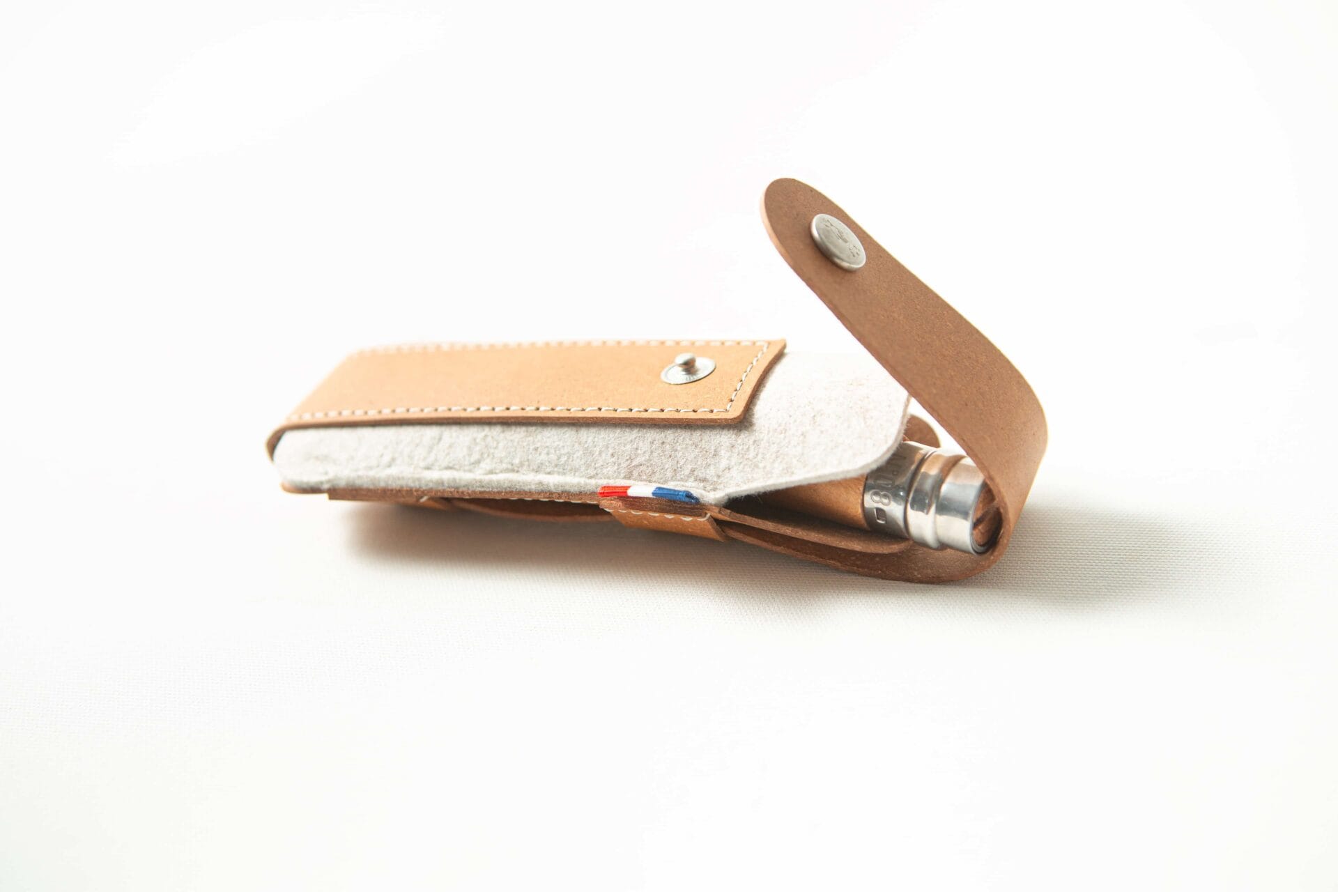 A brown Opinel Sheath, crafted from leather and felt with a press-stud fastening, is partially open to reveal a metal object inside.
