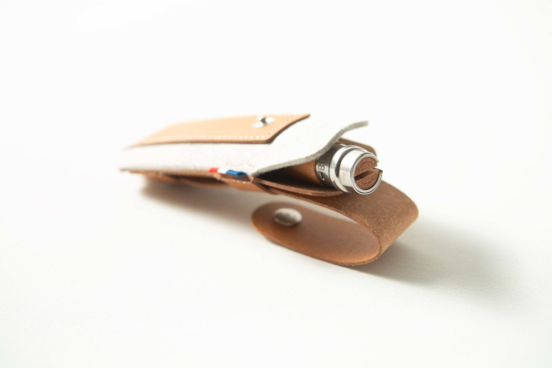 A brown Opinel Sheath holds a metallic pen, photographed on a white background.