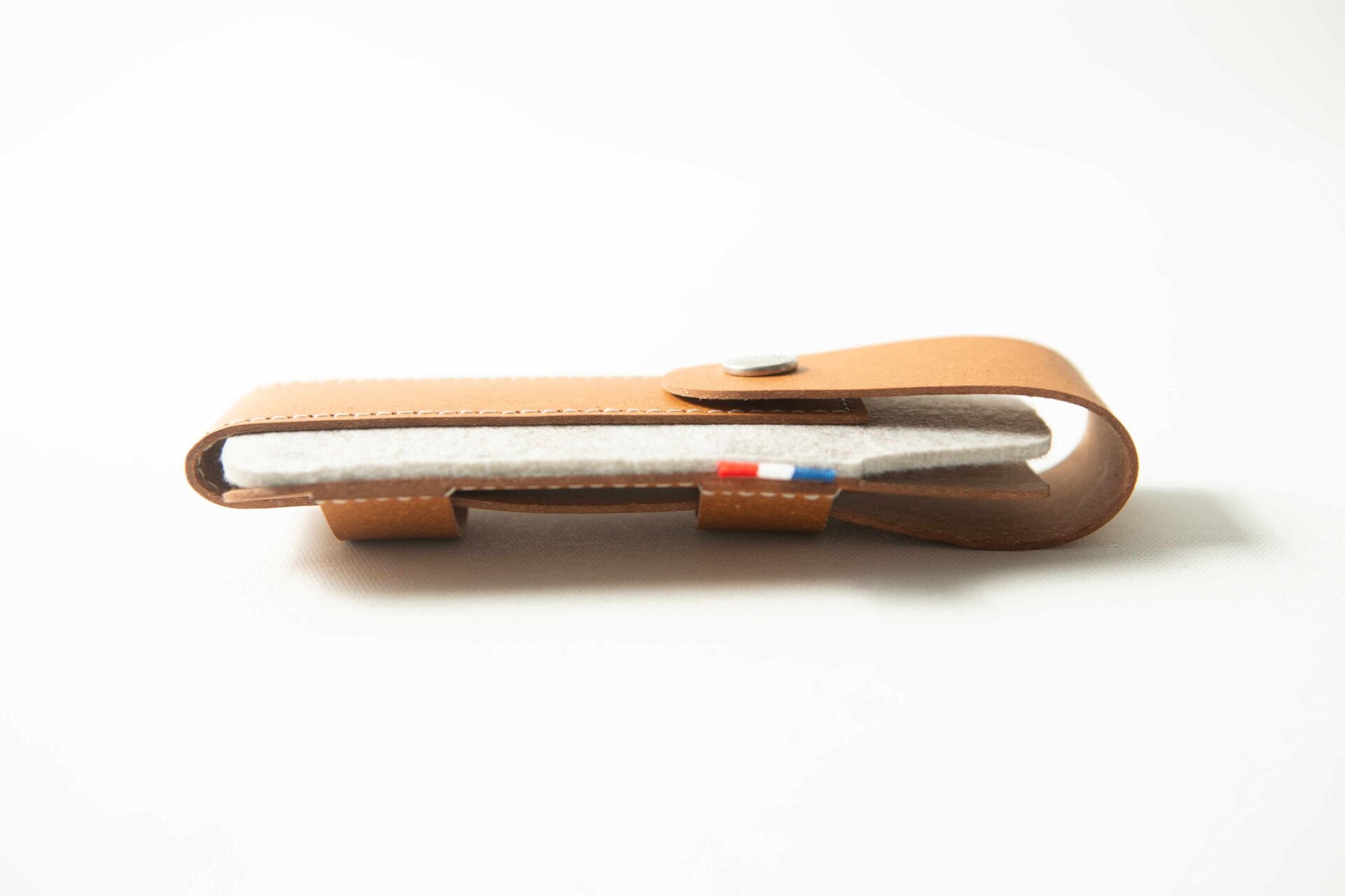 A brown leather Opinel Sheath with a buttoned flap, holding a white fabric item featuring a small coloured tag.
