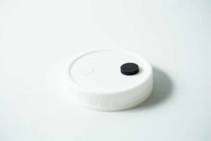 The Mycology premade Wide Mouth Mason Jar Lid is white with an injection port and air filter, featuring a textured surface—perfect as an autoclavable lid for liquid culture.