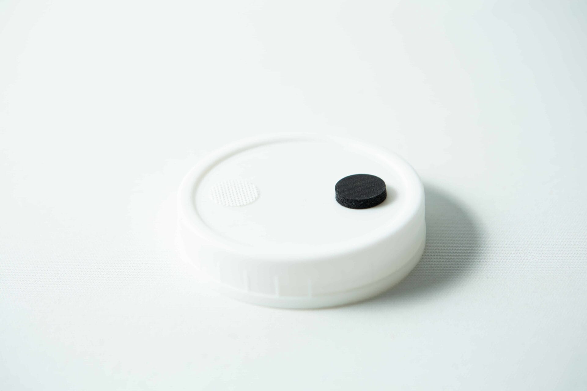 The Mycology premade Wide Mouth Mason Jar Lid is white with an injection port and air filter, featuring a textured surface—perfect as an autoclavable lid for liquid culture.