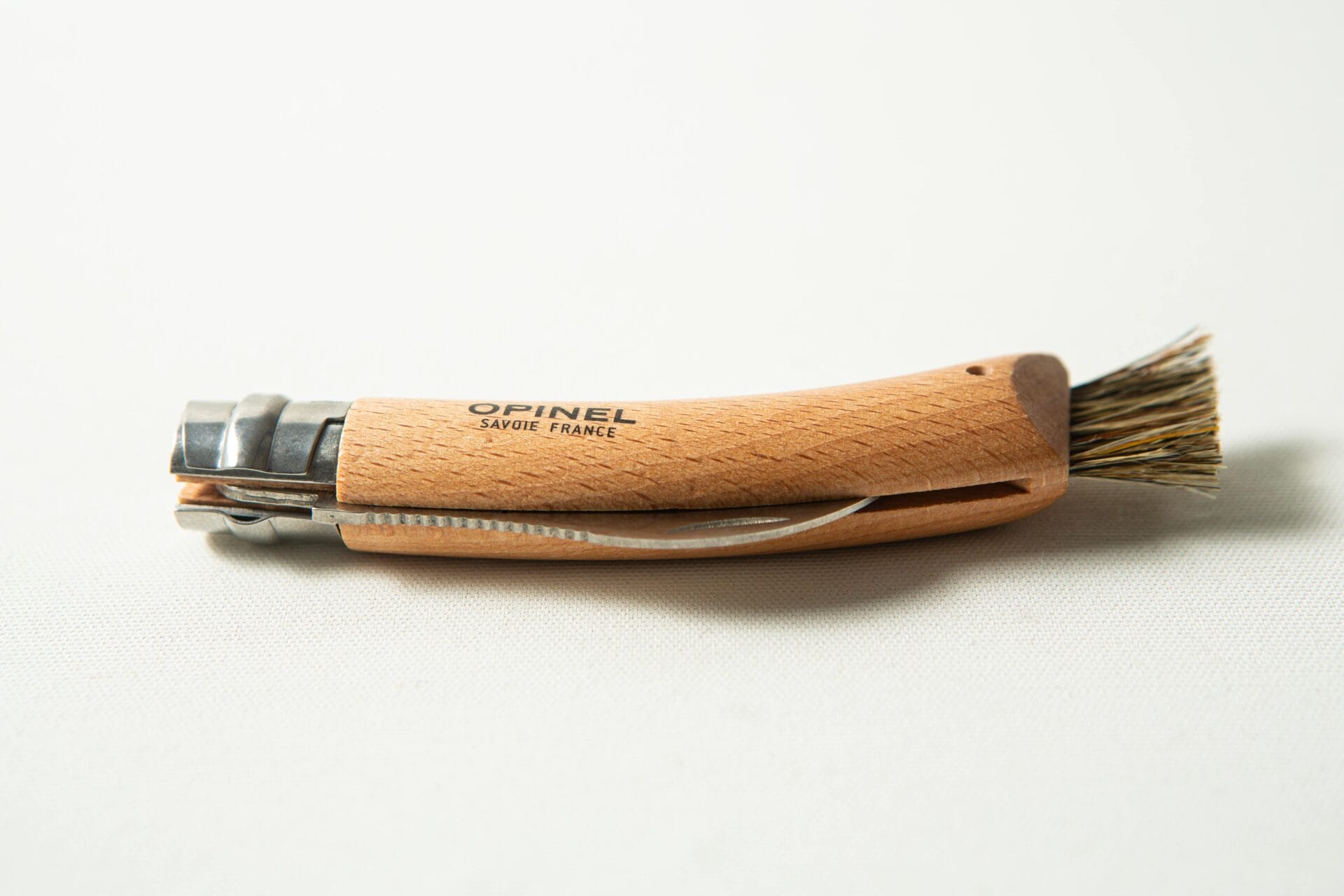 An Opinel No 8 Folding Mushroom Knife with a beech handle and stainless steel blade rests on a white surface.