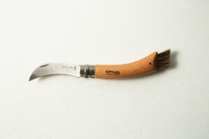 The Opinel No 8 Folding Mushroom Knife features a stainless steel blade, a beechwood handle, and a small brush—ideal for foraging and cleaning mushrooms.