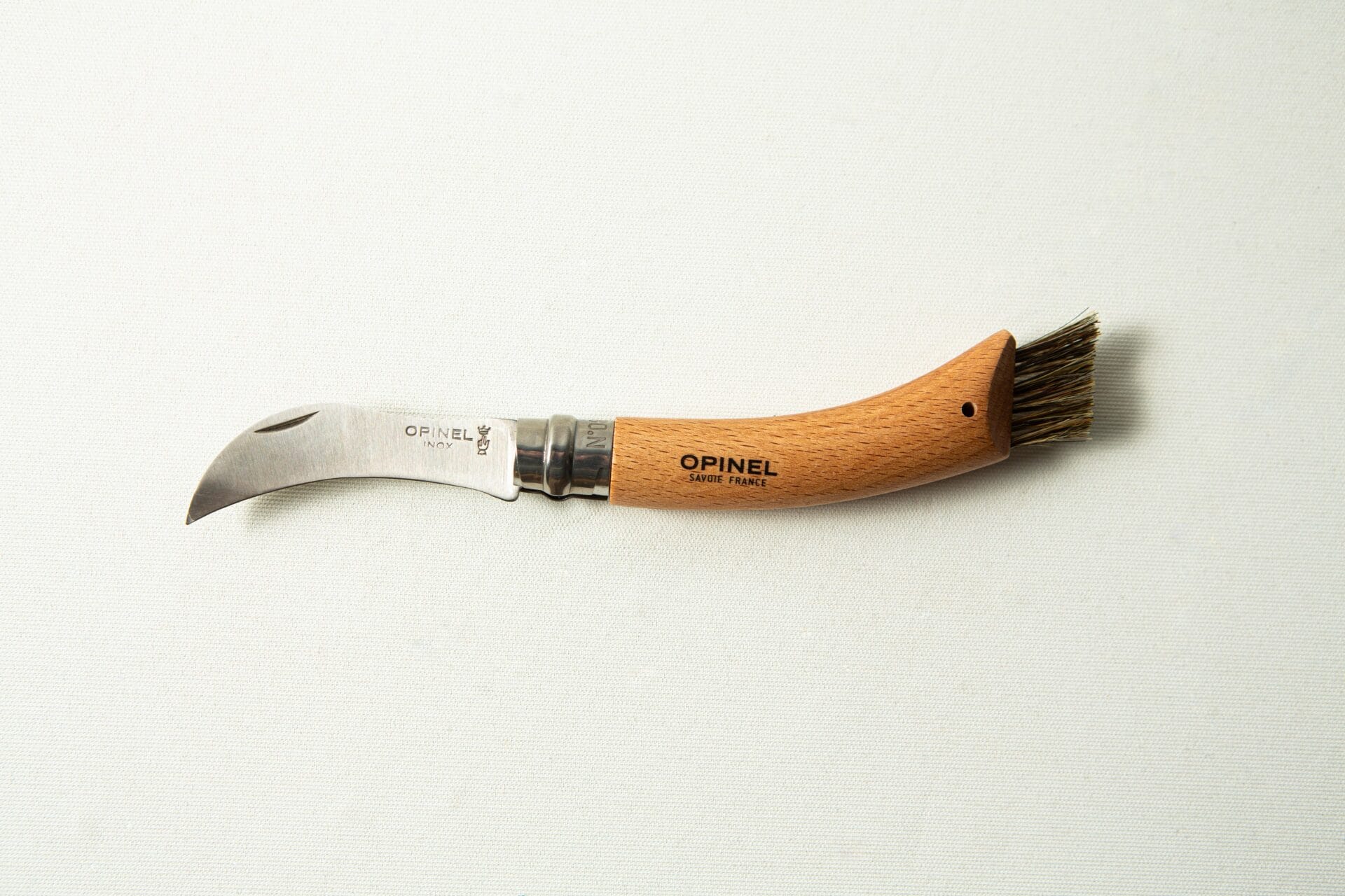 The Opinel No 8 Folding Mushroom Knife features a stainless steel blade, a beechwood handle, and a small brush—ideal for foraging and cleaning mushrooms.