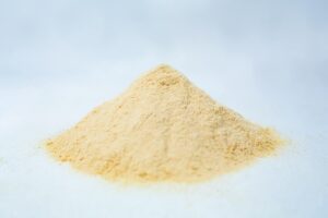 A small mound of fine, light yellow Mycological Soya Peptone powder for agar media use in microbiology labs rests on a white surface against a soft, blurred background.