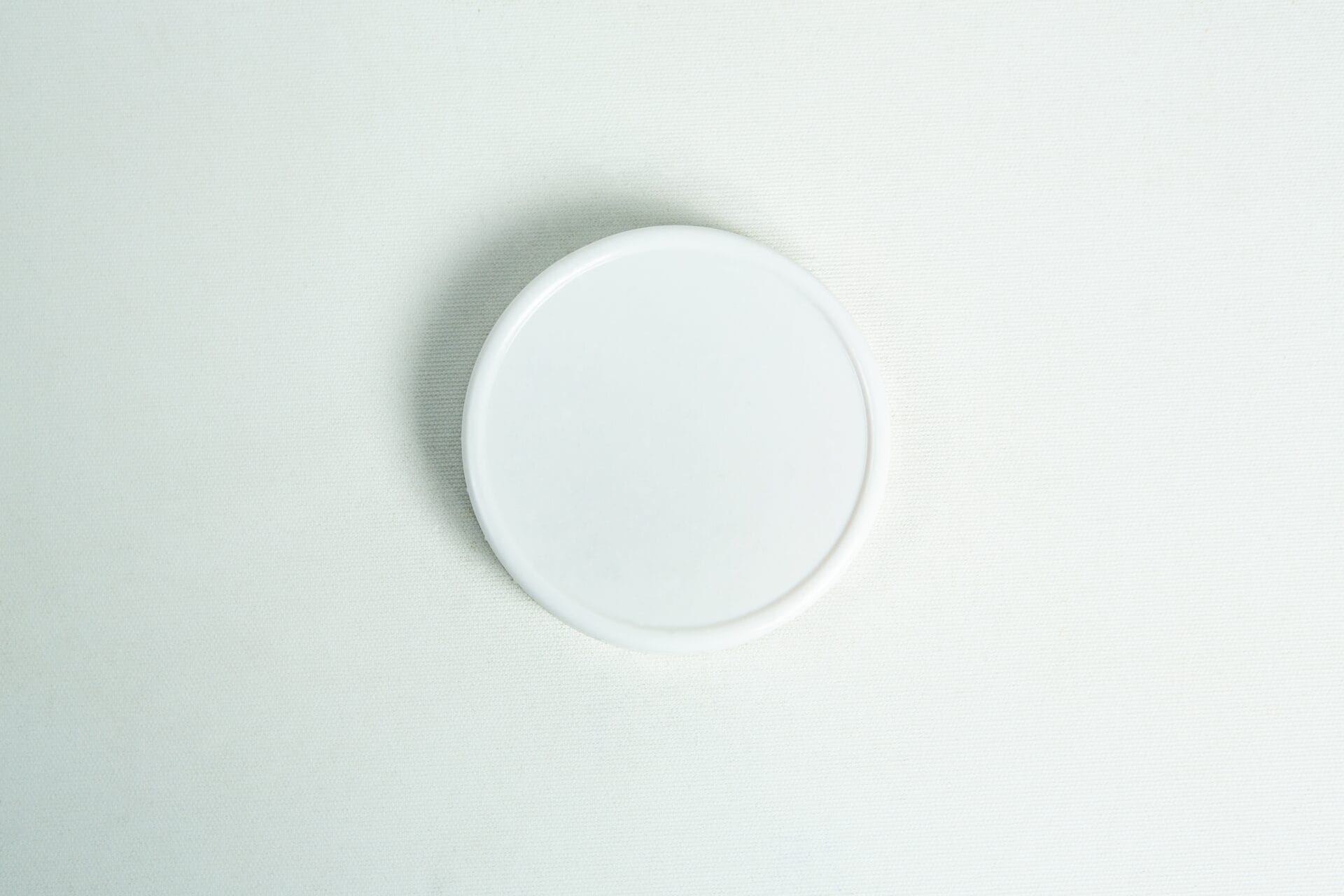 A plain white, wide-mouth 86mm plastic Mason jar lid rests on a simple white surface.
