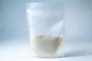 A clear resealable plastic pouch containing Natural Gypsum coarse grade—white granules used as a mushroom supplement for grain and substrate—stands upright on a light background.