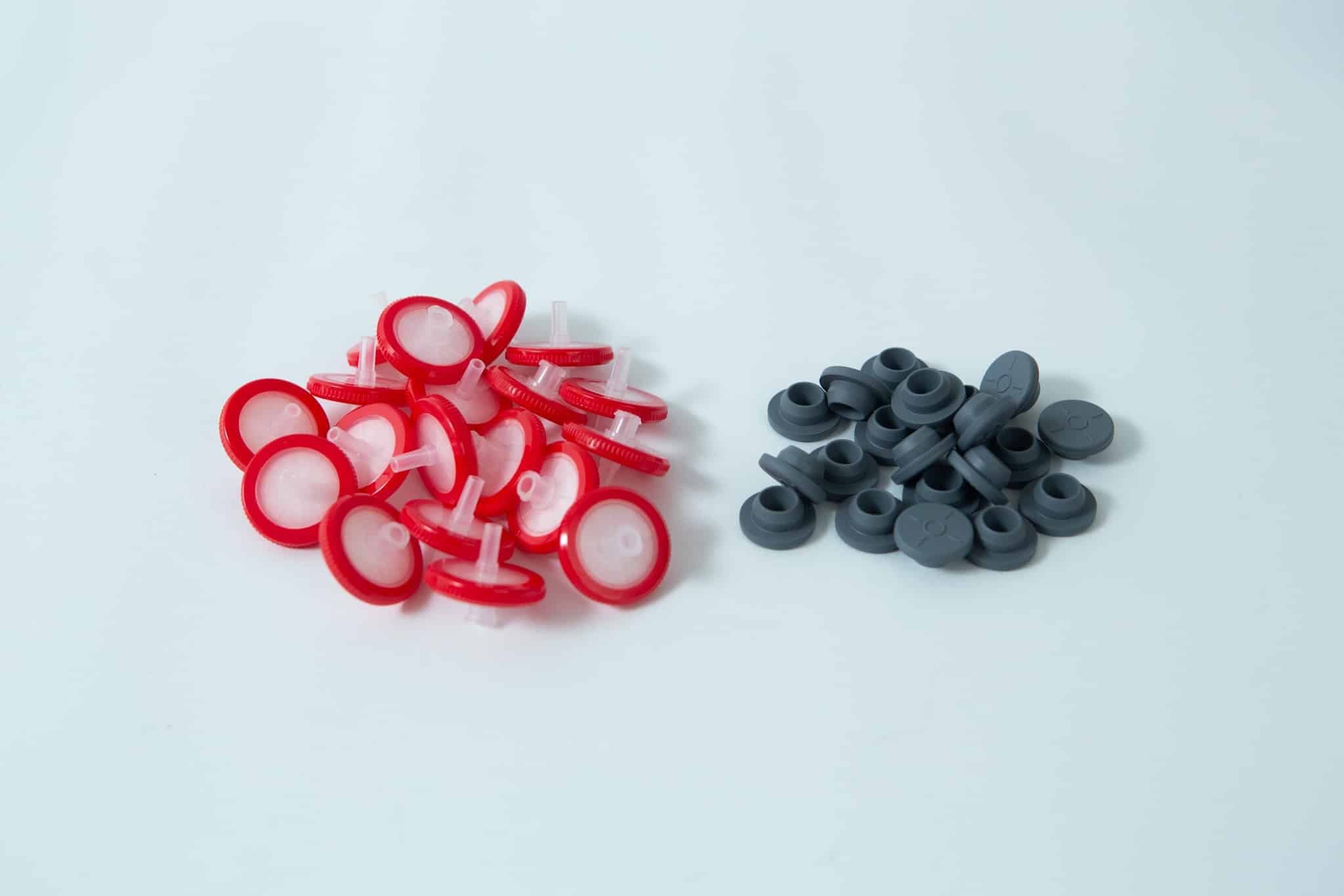 A set of Rubber Self-Healing Injection ports and red-and-white PTFE Syringe Filters for Mycology are arranged together on a white surface.