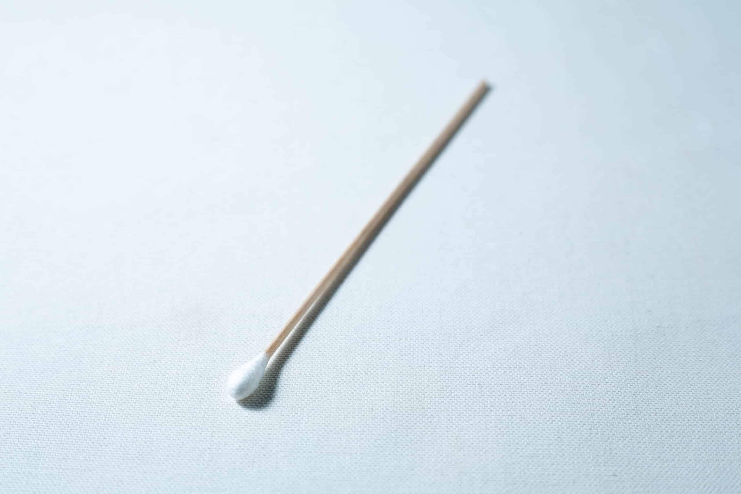 A single sterile cotton wool bud with a wooden stick is placed on a white surface.