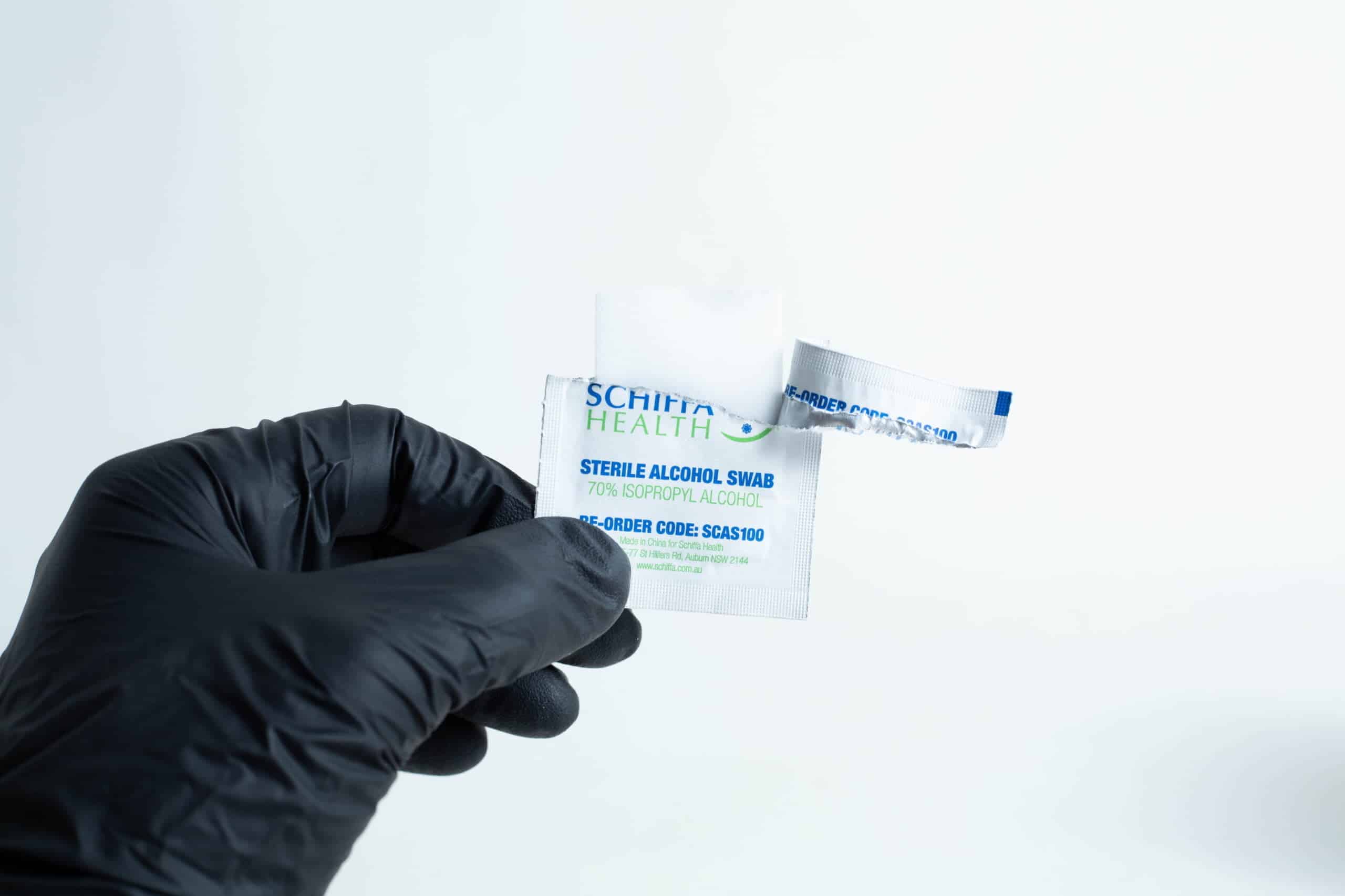 A hand in a black glove holds an open packet of Sterile Alcohol Wipes / Swabs / Pads (Box of 100) against a white background.