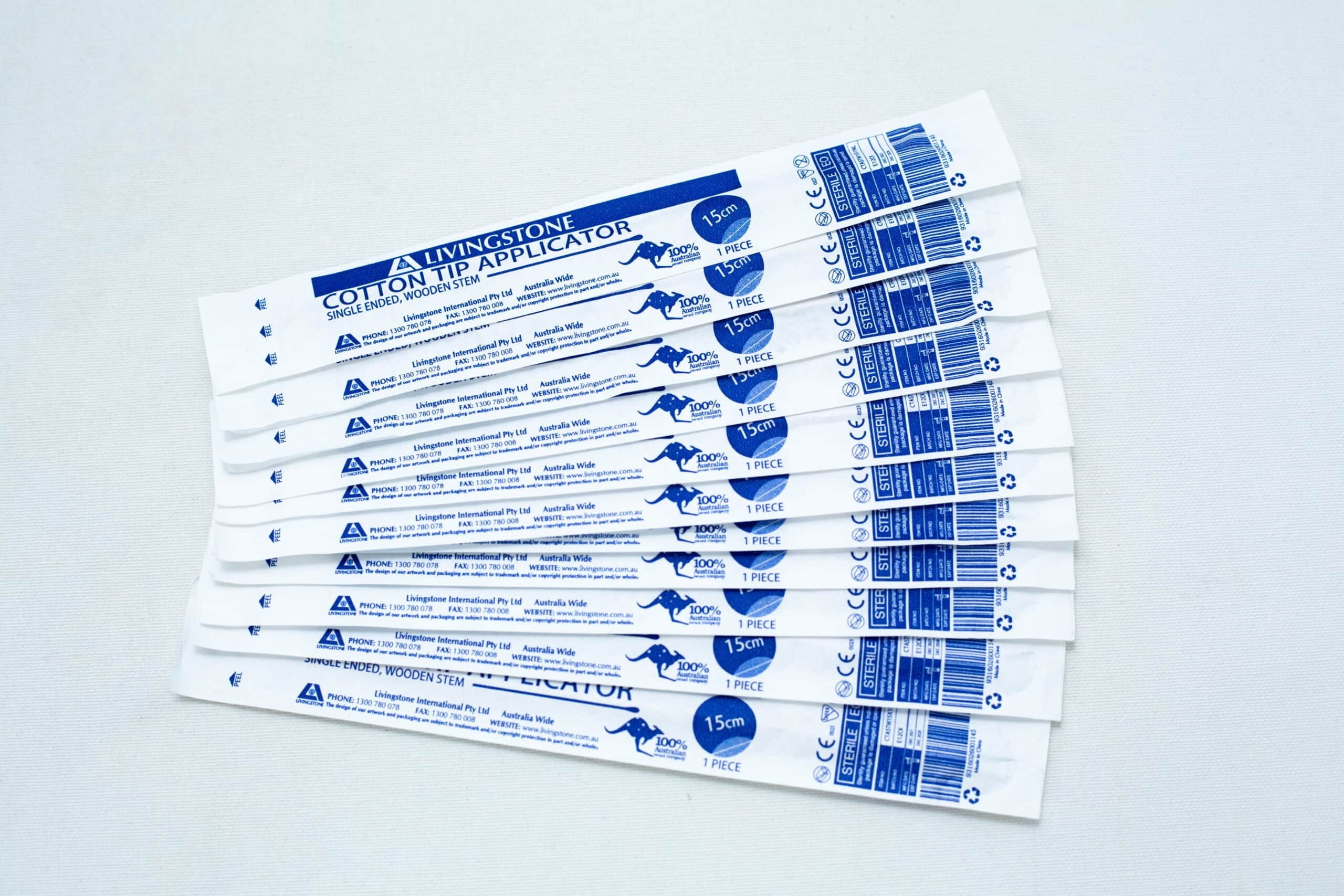 Ten packaged sterile cotton tip applicator/swab are fanned out on a white surface.