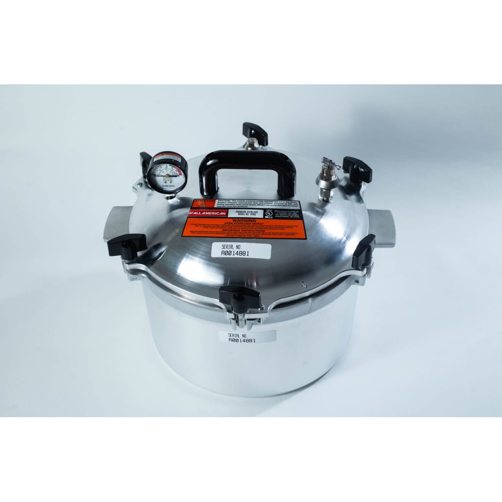 A stainless steel pressure cooker with a pressure gauge, black handles, and warning labels on the lid.