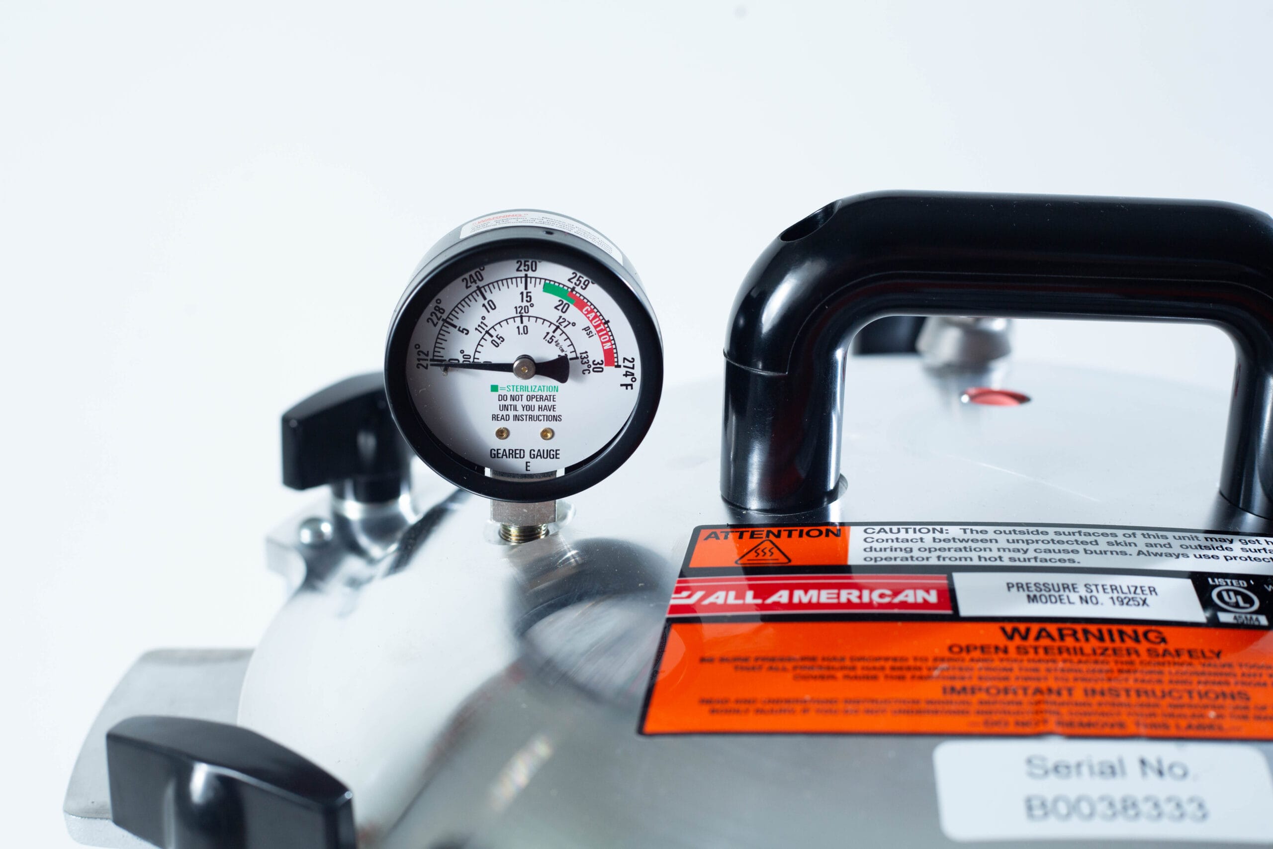 Close-up of a pressure gauge and warning labels on a stainless steel pressure steriliser.