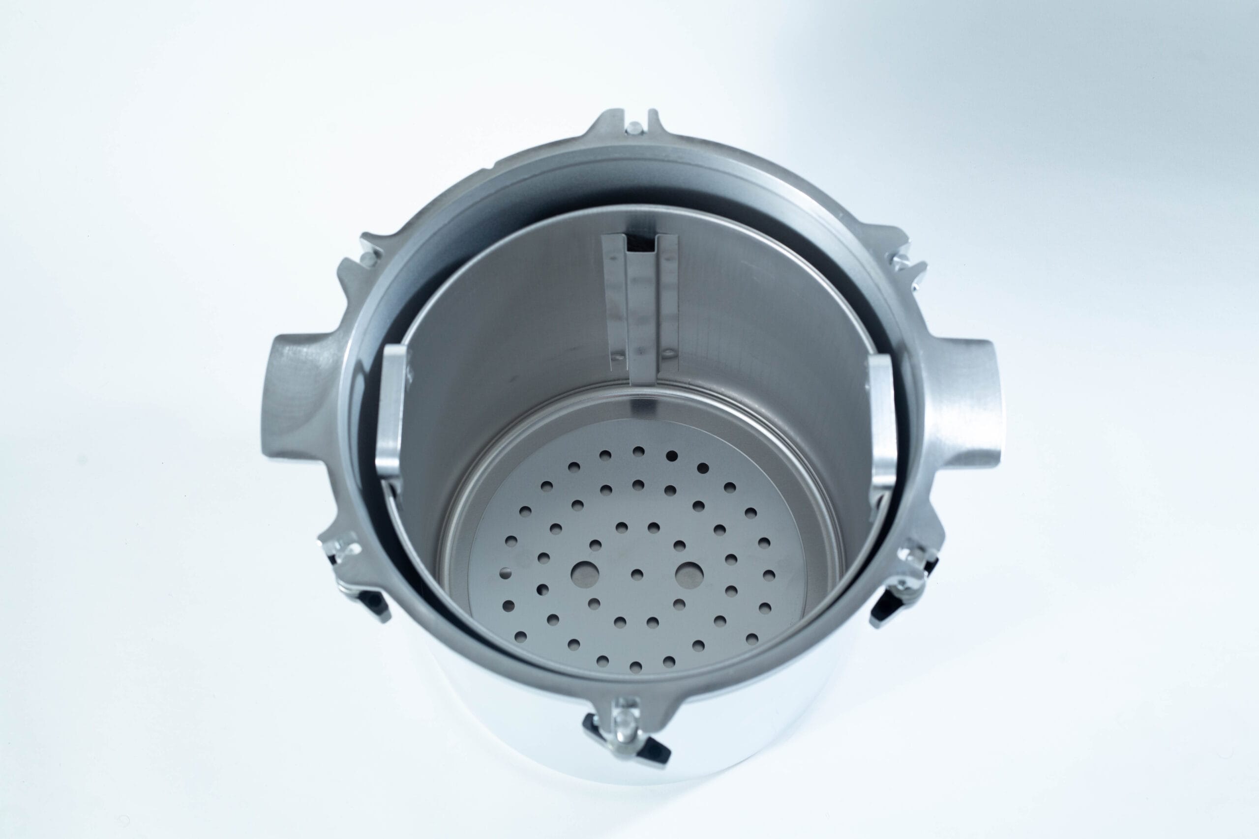 Top view of an empty stainless steel autoclave chamber with a perforated metal tray inside.