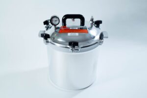 A stainless steel pressure cooker with a gauge, handle, and safety valves on a white background.