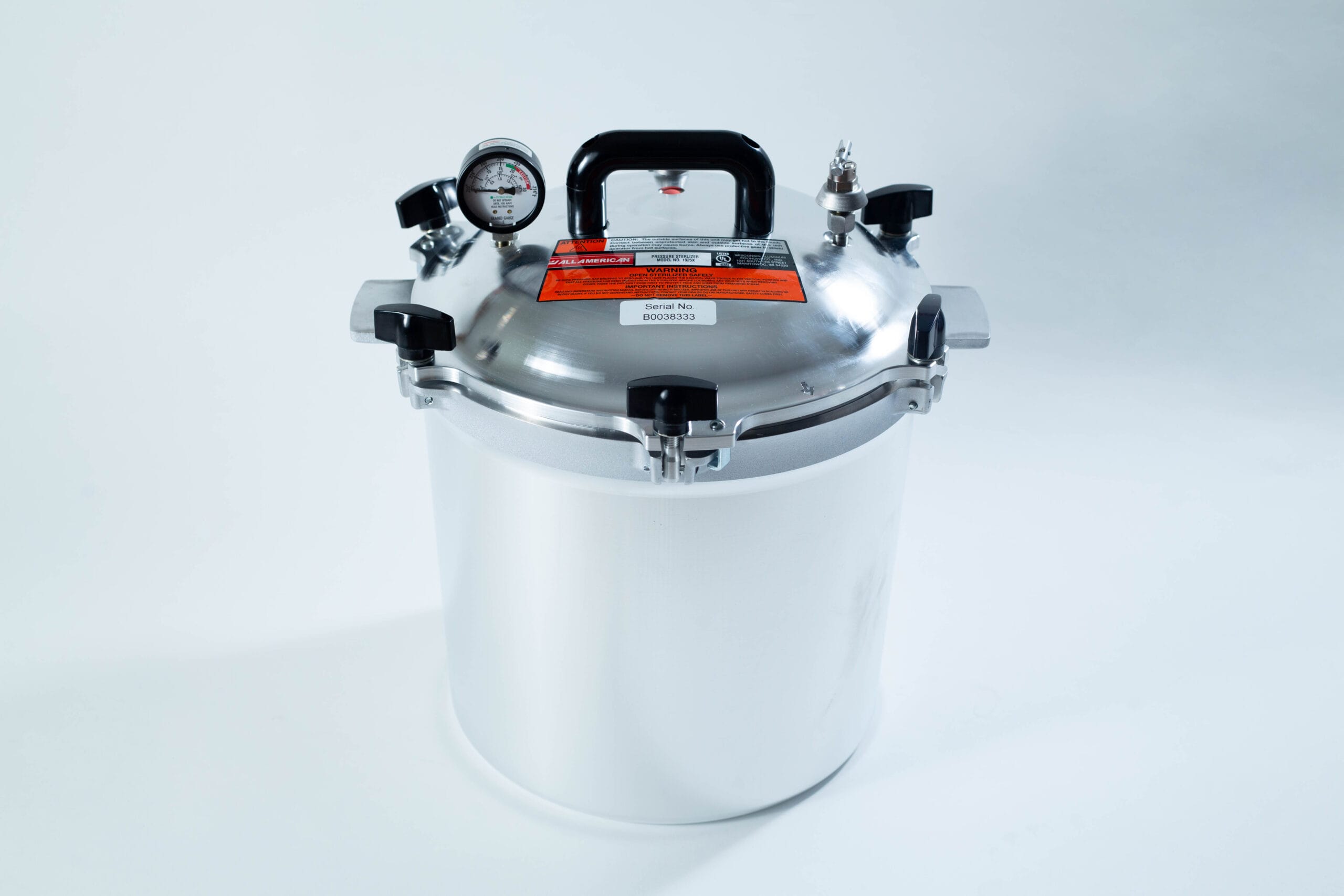 A stainless steel pressure cooker with a gauge, handle, and safety valves on a white background.